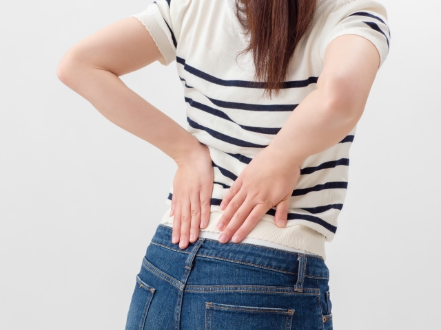 腰に手を当ててつらそうにしている女性
